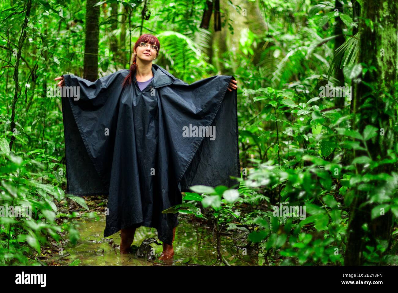 Touristenfrau Im Amazonischen Dschungel, Die Typische Ausrüstung Und Bekleidung Für Diese Umgebung Zeigt, Regen Poncho Und Gummistiefel Stockfoto