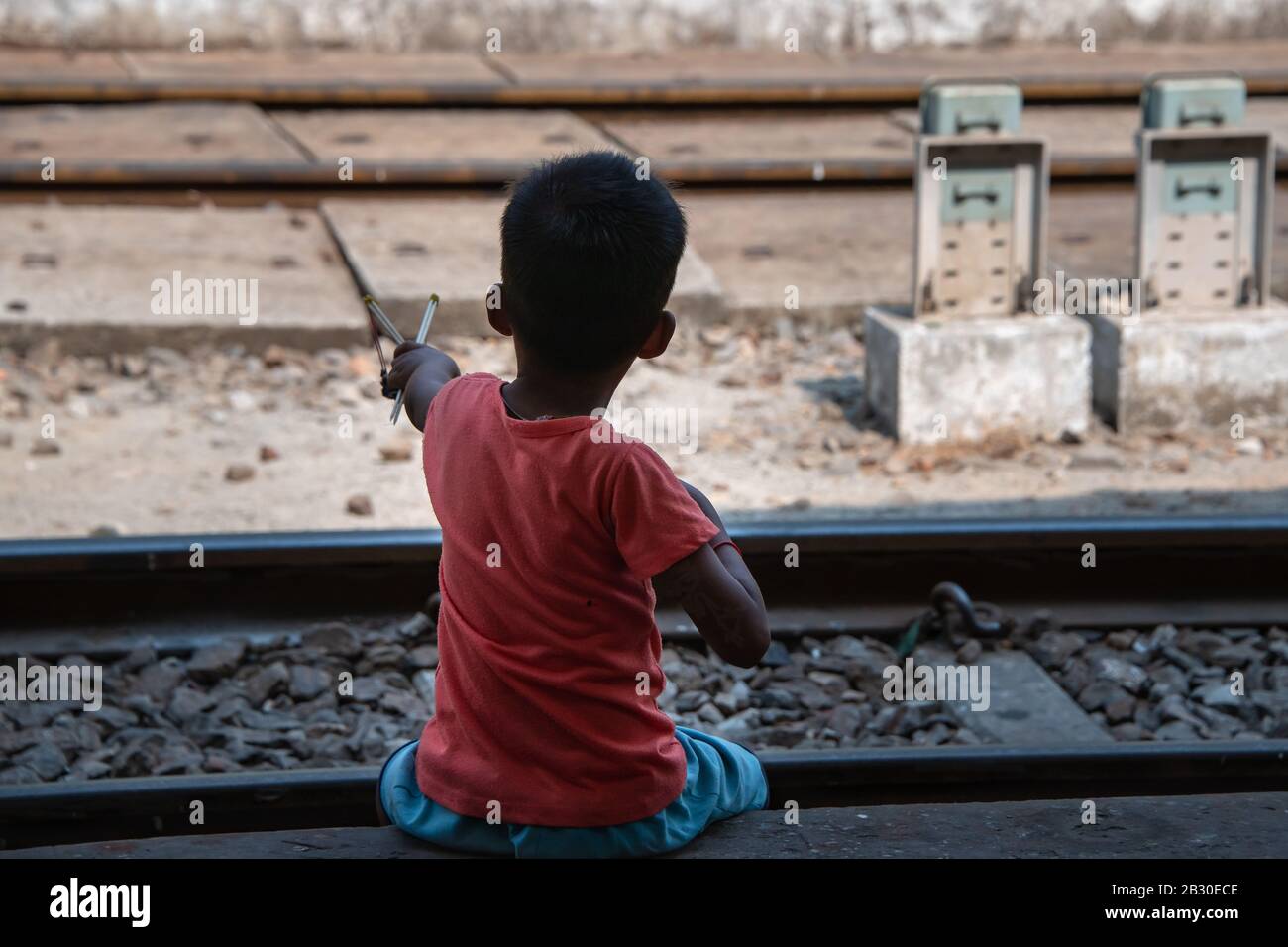 Yangon, Myanmar - Januar 2020: Junger asiatischer Junge, der mit einem einfachen hausgemachten Katapult neben Bahngleisen spielt, Stockfoto