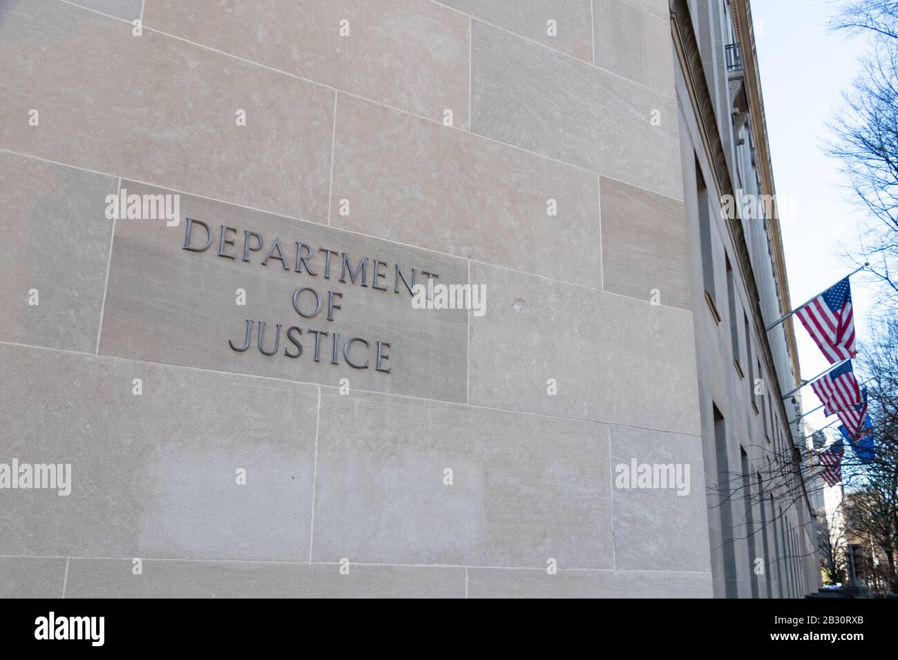 Text des Justizministeriums auf der Seite des Hauptquartiers in Washington, D.C. - amerikanische Flaggen im Hintergrund. Stockfoto