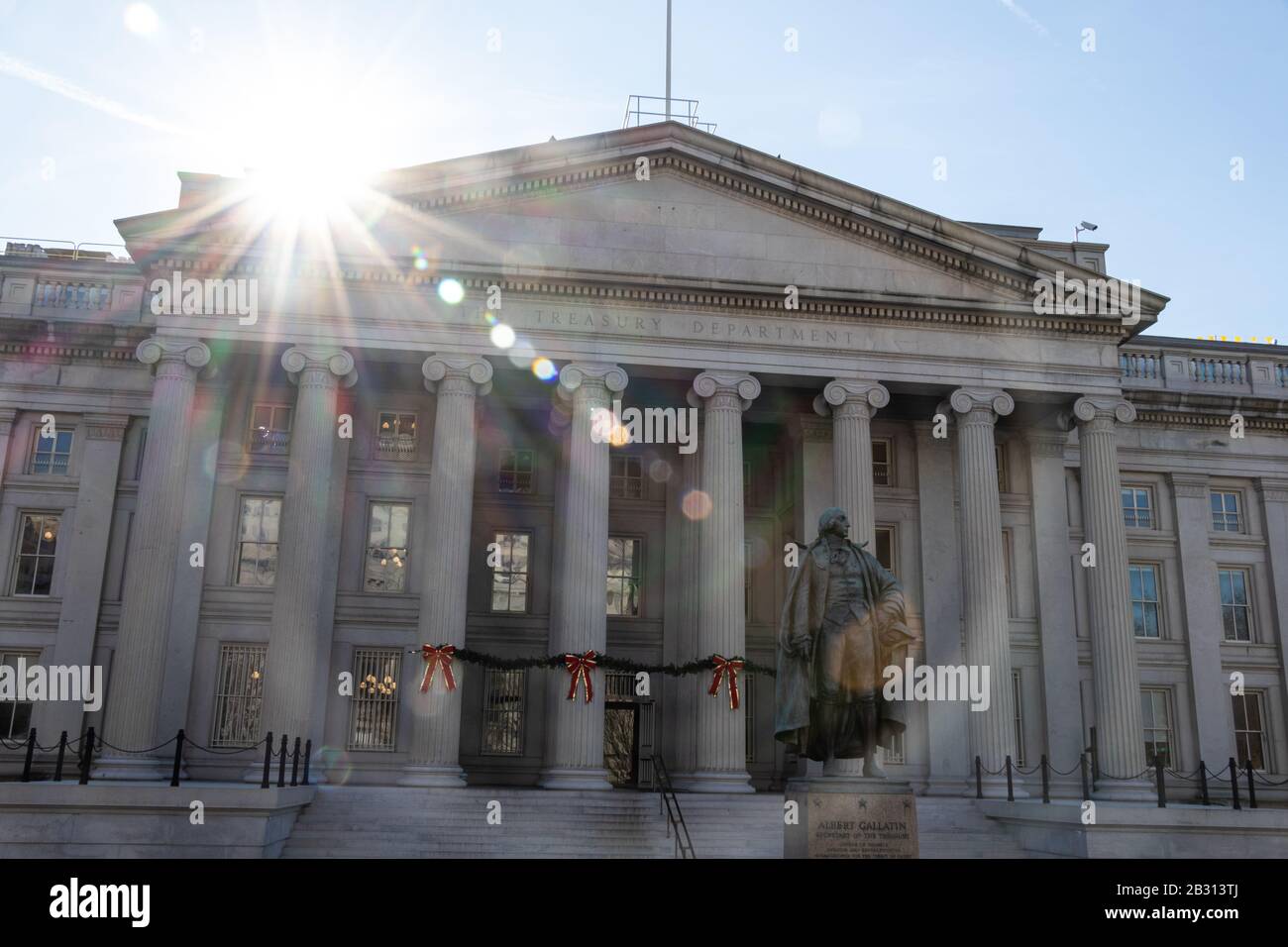 Die Sonne krampft auf das Treasury Building, in dem das US-Finanzministerium ansässig ist. Bronzestatue an Albert Gallatin im Vorderteil. Stockfoto