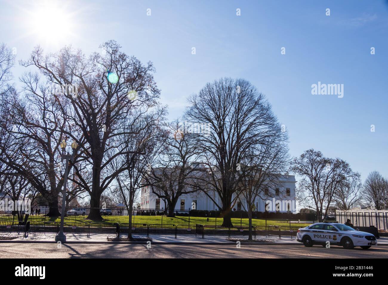 Die Sonne, die auf der Pennsylvania Avenue als Secret Service Fahrzeug hinunterscheint, wird vor dem Weißen Haus im Hintergrund hinter dünnen Bäumen geparkt. Stockfoto