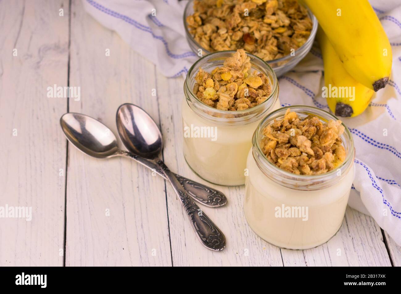 Joghurt mit Bananen und Granola auf weißem Holzhintergrund. Frühstück, Dessert. Stockfoto
