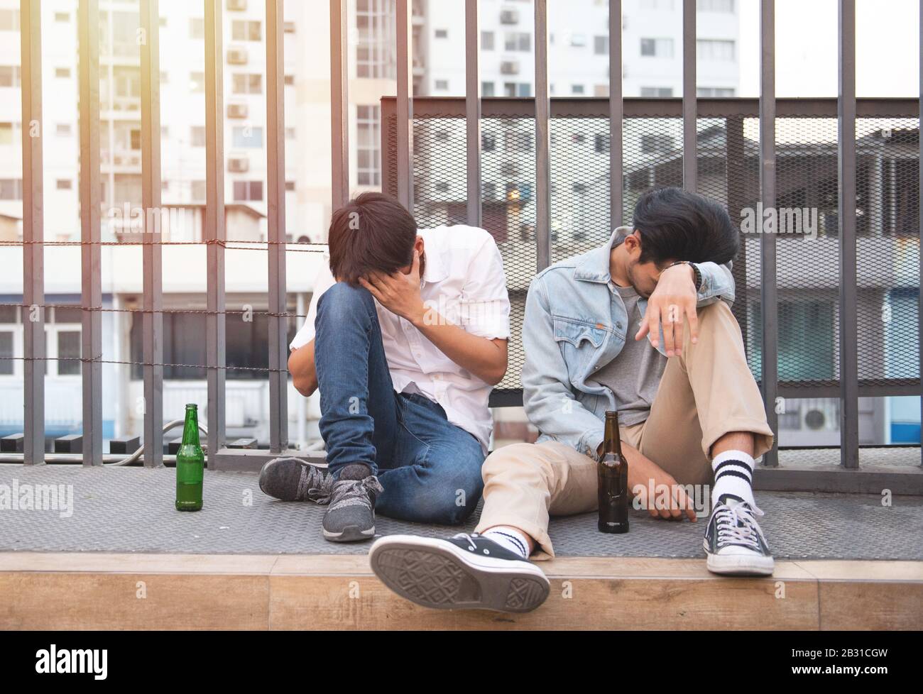 Zwei junge Männer betrunken und sitzen schlafend auf der Straße mit einer Flasche Bier in unglücklicher. Stockfoto