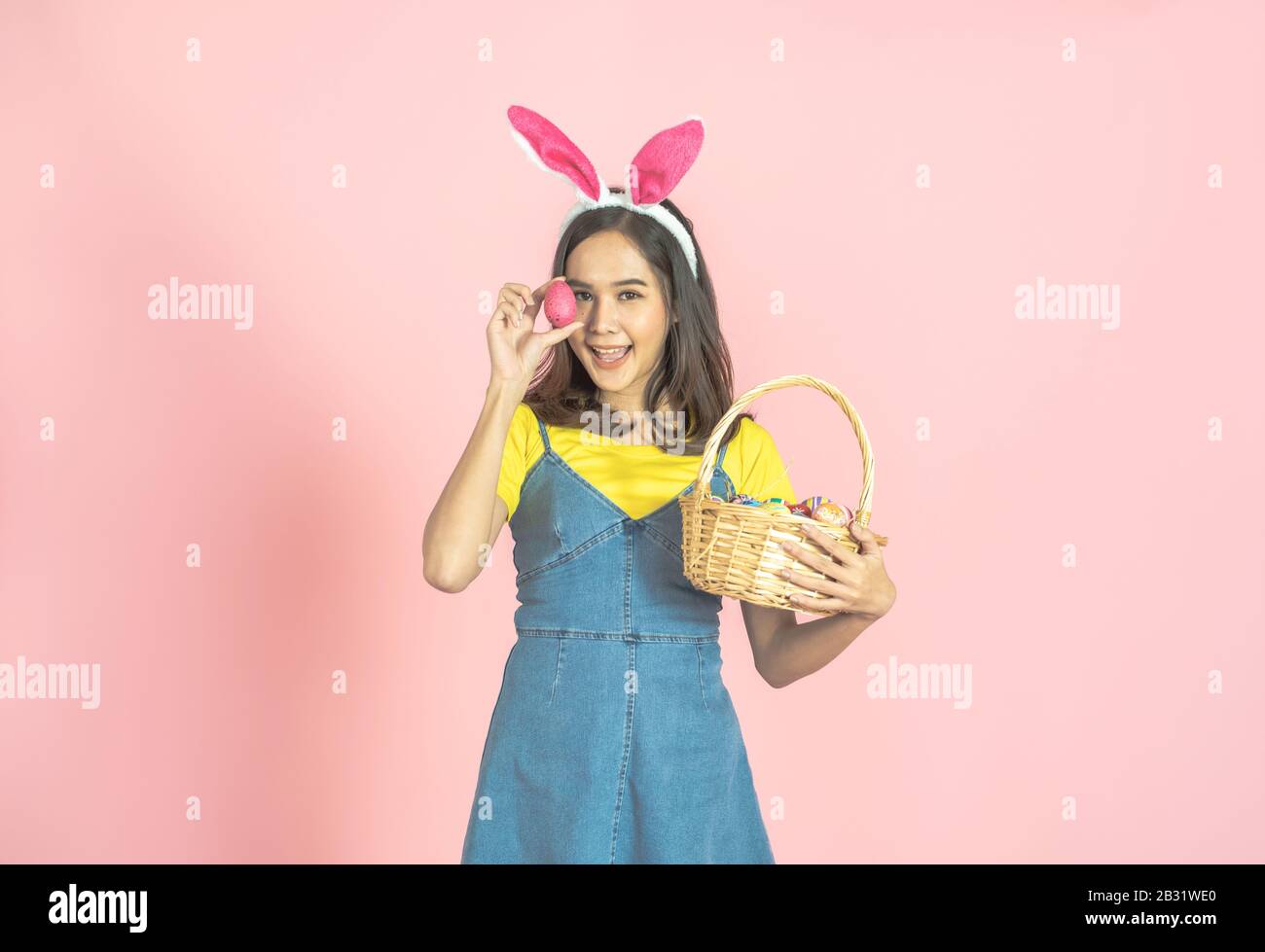 Studio von asiatischer Schönheit fröhliche junge Frau, die bunte Ohren trägt und buntes Osterei vor ihrem Auge schön hält. Stockfoto