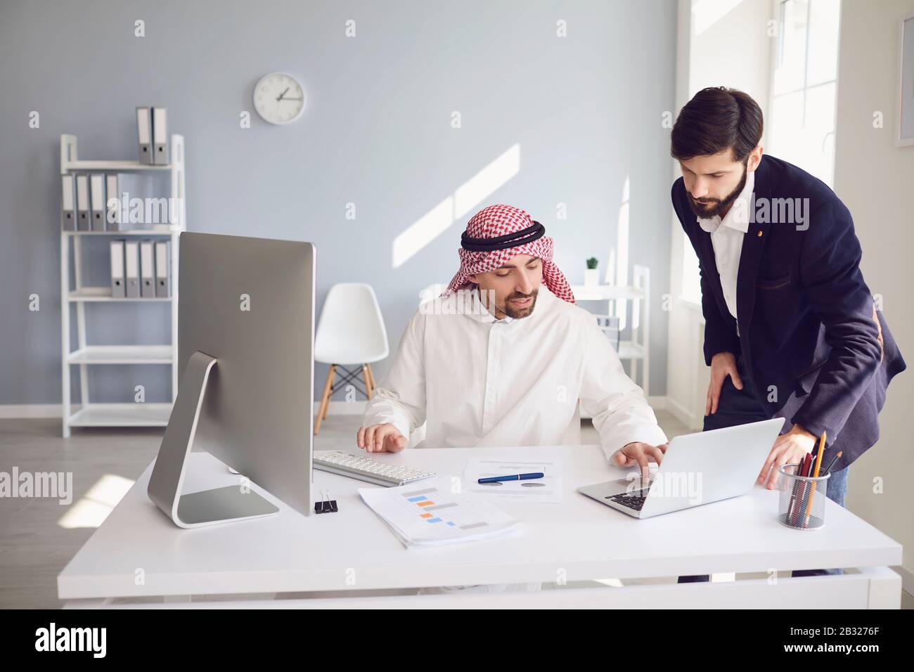 Arabische und europäische Unternehmer arbeiten zuversichtlich in einem weißen Büro. Stockfoto