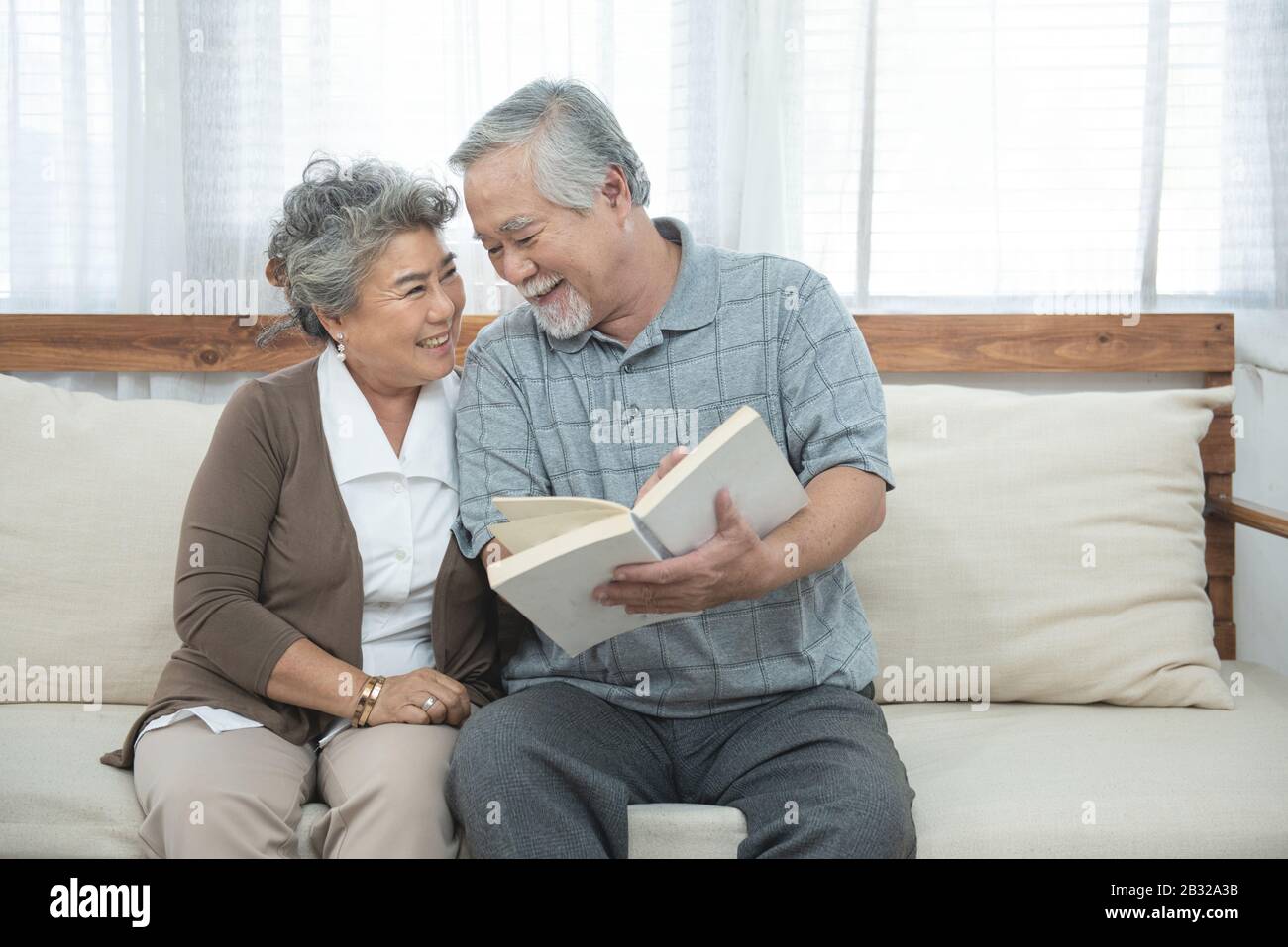 Älteres älteres asiatisches Paar sitzt zu Hause zusammen auf dem Sofa und liest Buch.Mutter Und Großvater verbringen Zeit zusammen im Haus. Stockfoto