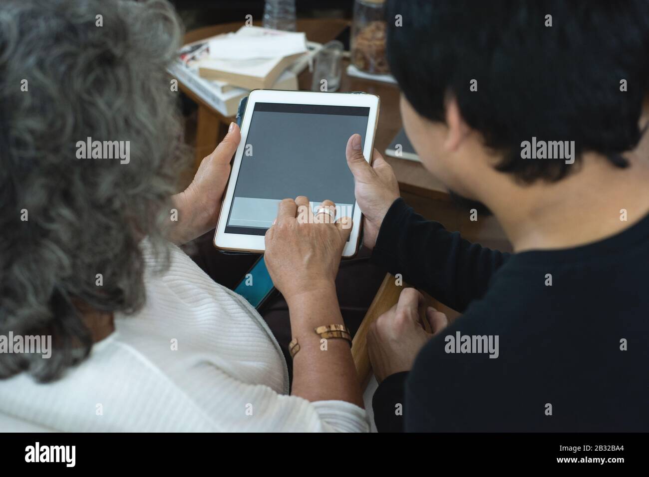 Rückansicht der älteren älteren älteren älteren älteren asiatischen Frau, die die Anwendung zur Gesundheitsüberwachung auf einem digitalen Tablet verwendet, während sie zusammen mit Grandson im Wohnzimmer versammelt ist Stockfoto