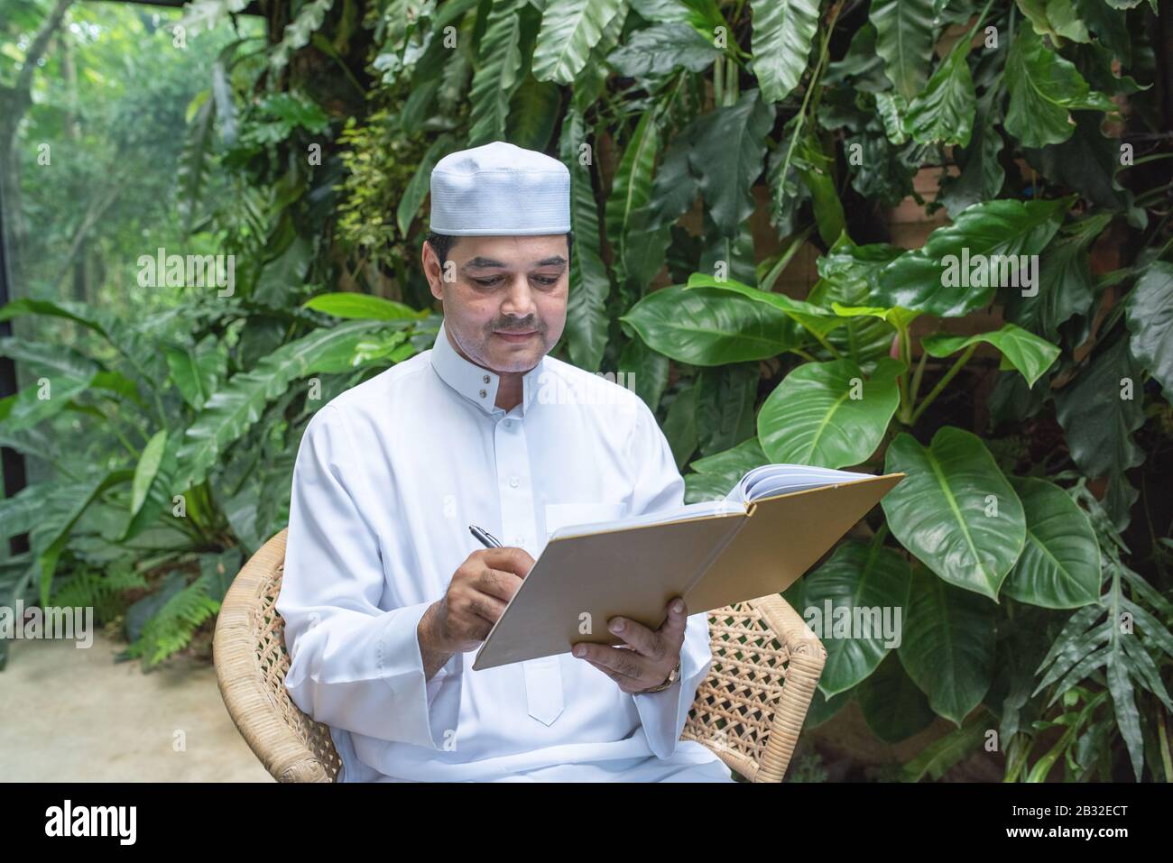 Saudi-muslimischer Mann kleidet hijab sitzen und schreiben auf Lehrbuch, freiberufliches Geschäftskonzept. Stockfoto