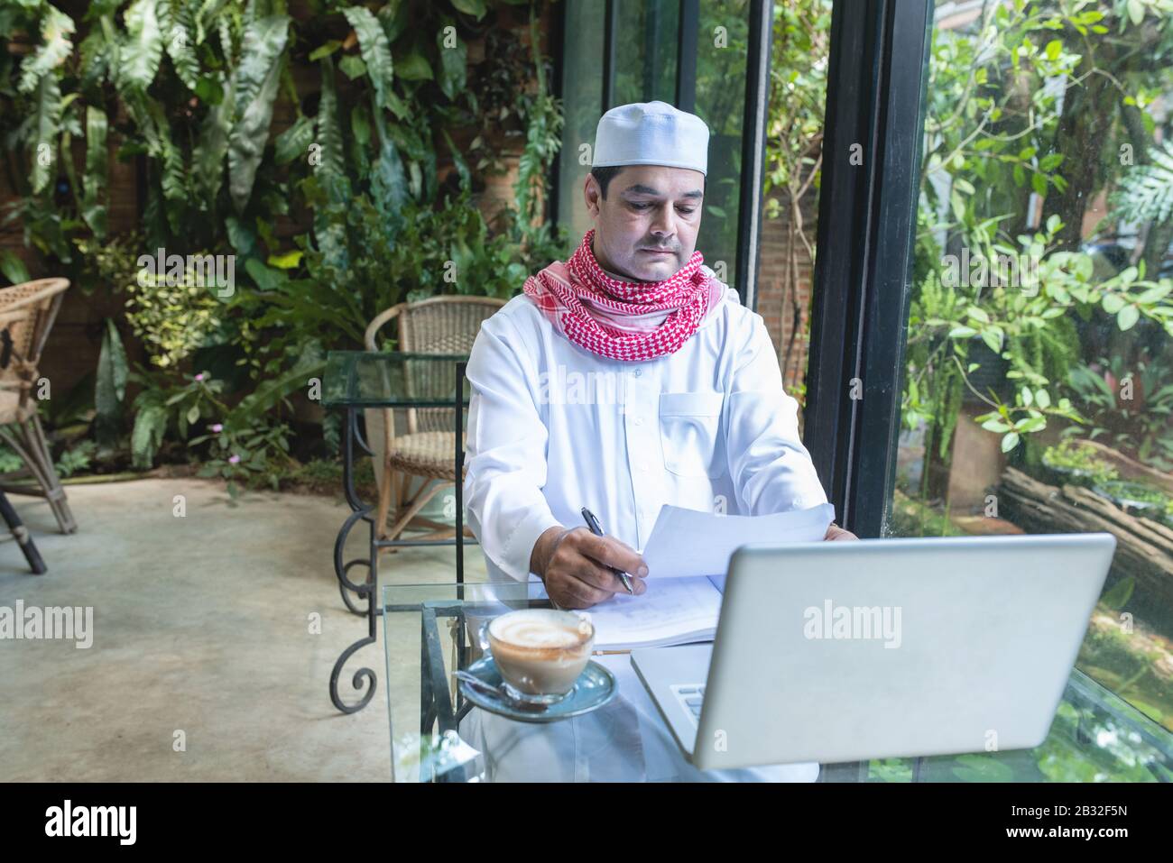 Junge gutaussehende arabische geschäftsleute im Café mit gekleideten Hijab sehen sich Papierakte mit Laptop auf dem Tisch an. Stockfoto