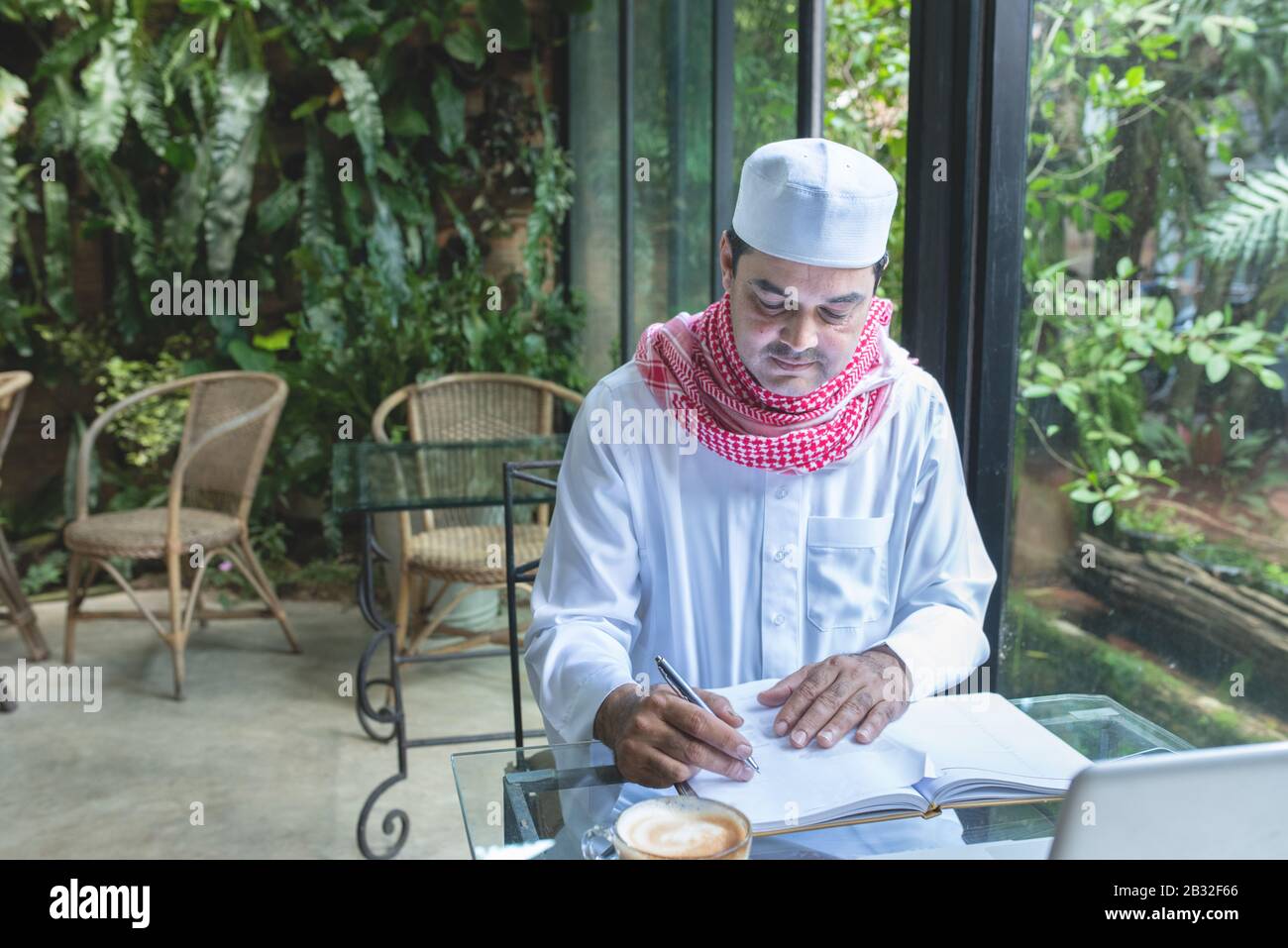 Junge, gutaussehende Geschäftsleute arabischer muslime in einem Café mit Hijab, die gekleidet sind, schreiben auf eine Buchdatei mit Laptop auf dem Tisch. Stockfoto