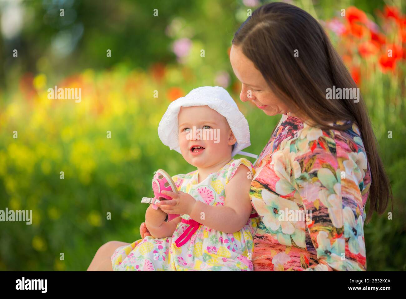 Fröhliche Frau und Kind auf der Mohnwiese. Mutter und Tochter spielen, umarmen und lächeln. Familienurlaub und Zusammengehörigkeit. Glückliche Familie, die Outdoo spielt Stockfoto