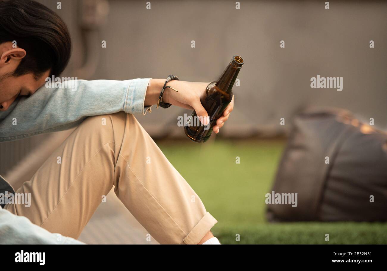 Sucht hungriger betrunkener Mann hält Flasche Bier in der Hand sitzen und inaktiven Schlaf.arbeitsloser junger asiat, der an Finanzproblemen leidet, aussichtslos Stockfoto