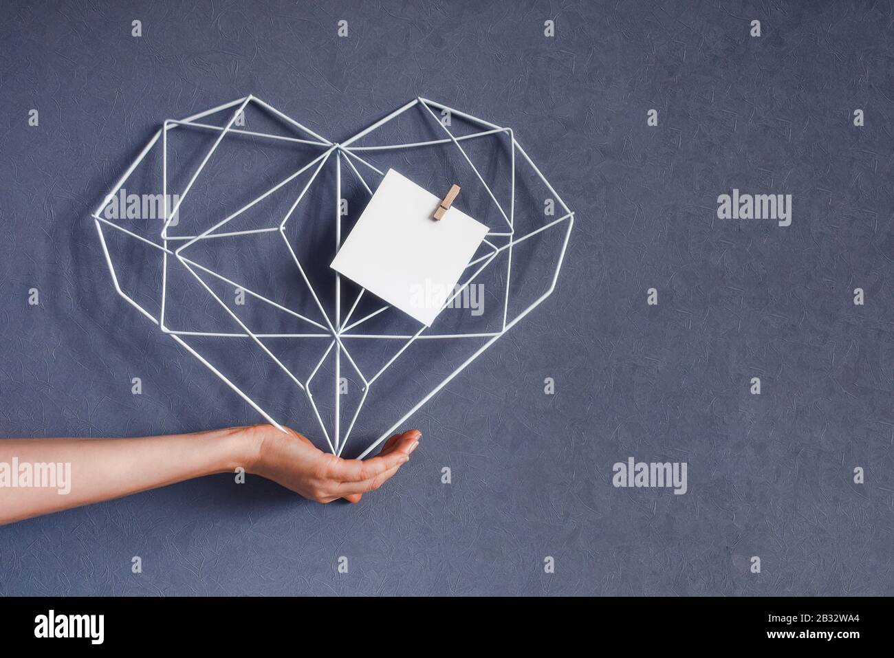 Moderner Rahmen in Form eines Herzens in der Hand auf dem Hintergrund einer grauen Wand. Inneneinrichtung Herzsymbol der Liebe Stockfoto