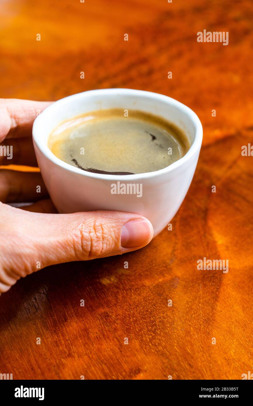 Nehmen Sie eine Tasse Kaffee in einem hübschen Café mit Hüftpfanne. Weich fokussiertes Bild. Tasse Espresso auf dem alten Holztisch der Cafeteria. Stockfoto