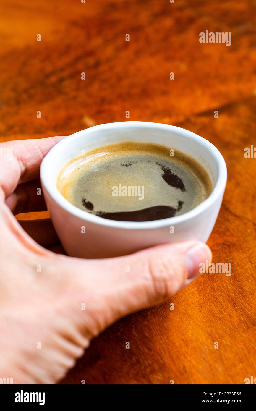 Nehmen Sie eine Tasse Kaffee in einem hübschen Café mit Hüftpfanne. Weich fokussiertes Bild. Tasse Espresso auf dem alten Holztisch der Cafeteria. Stockfoto