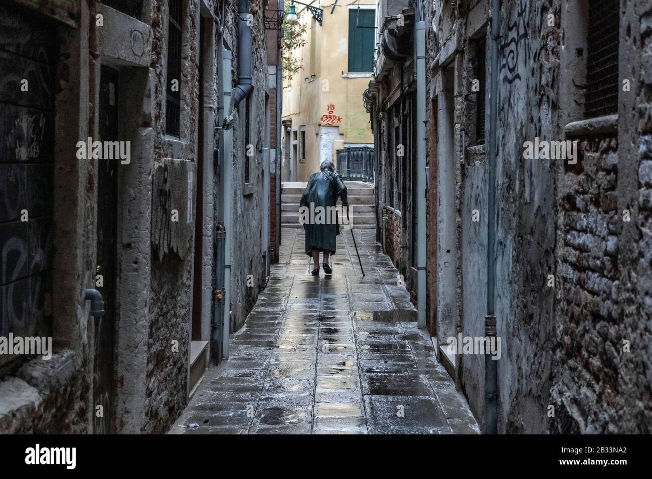 Alte Dame, die mit einem Spazierstock überschlagen wurde und allein durch die nassen Straßen von Venedig, Italien, spazieren ging Stockfoto