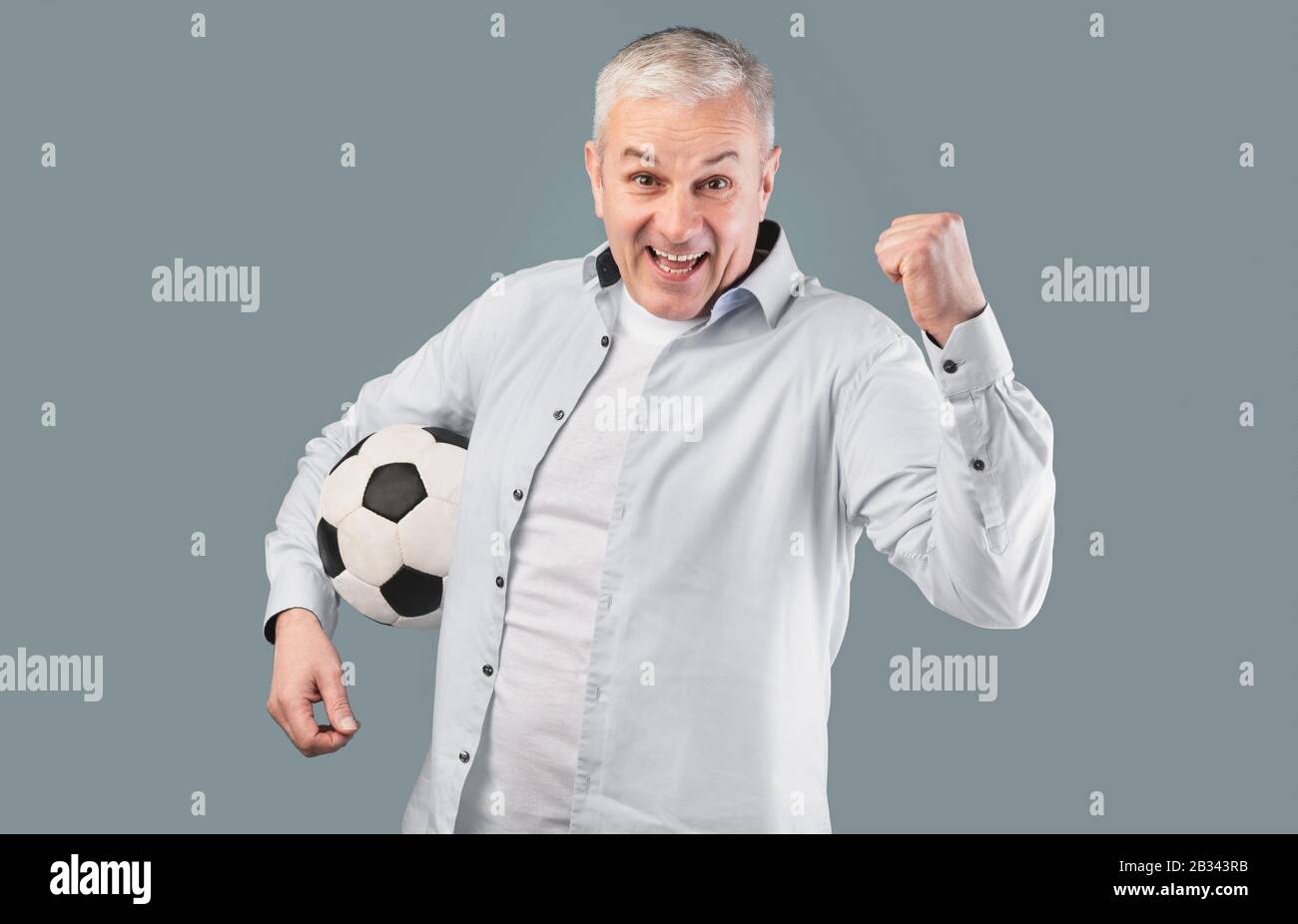 Mann posiert mit Fußball auf grauem Studiohintergrund Stockfoto