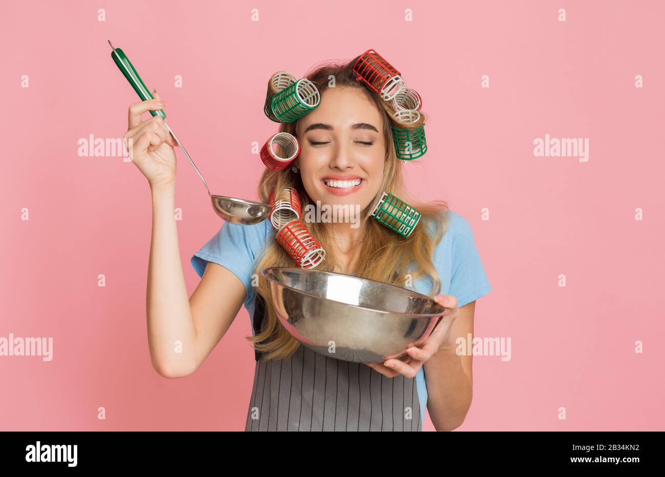 Hausfrau genießt Geschmack, hält Schüssel und Pfanne in der Hand Stockfoto