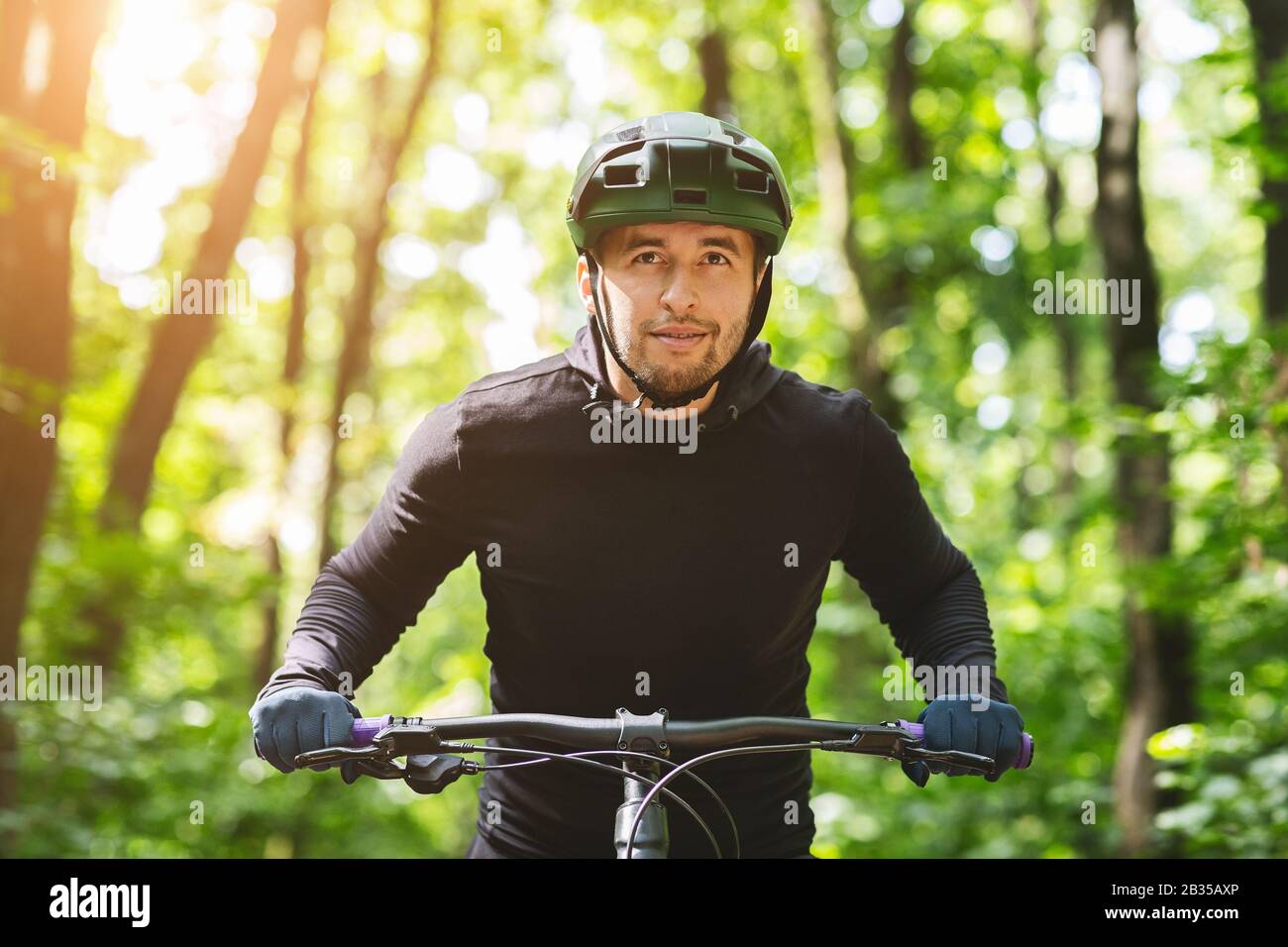 Ernsthafter Radfahrer, der in Sonnenschein auf dem Waldweg reitet Stockfoto