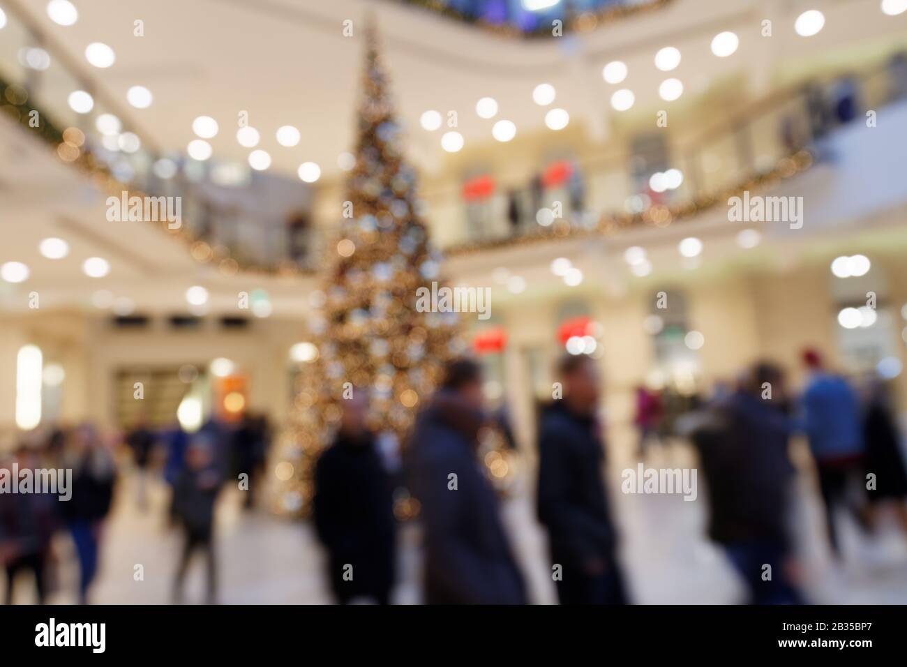 Christmas Shopping Circus: Verschwommene Szene mit dandernden Fußgängern rund um Christmas Decoration Tree in der Shopping Mall Stockfoto