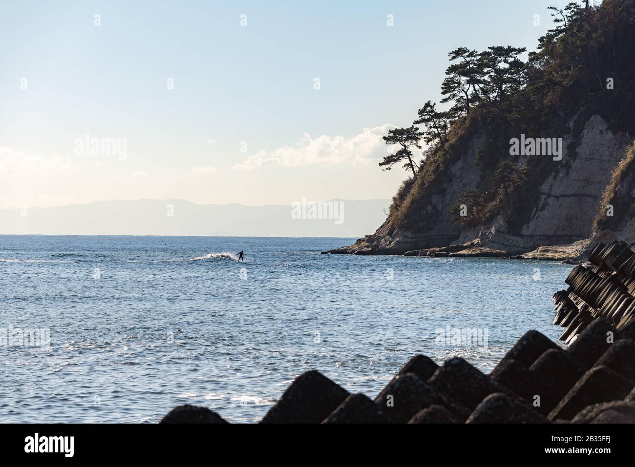 Ein Surfer reitet eine Welle in Richtung Kap Imamuragasaki, Sagami-Bucht, in der Nähe der Insel Enoshima, und stellt die Segelveranstaltungen der Olympischen Sommerspiele in Tokio 2020 vor Stockfoto