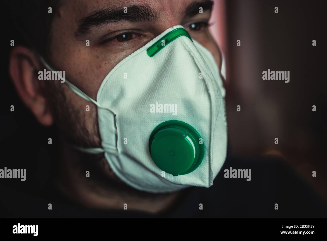 Detail der Atemschutzmaske auf dem Gesicht des mit Corona-Virus infizierten Mannes, rote Augen Stockfoto