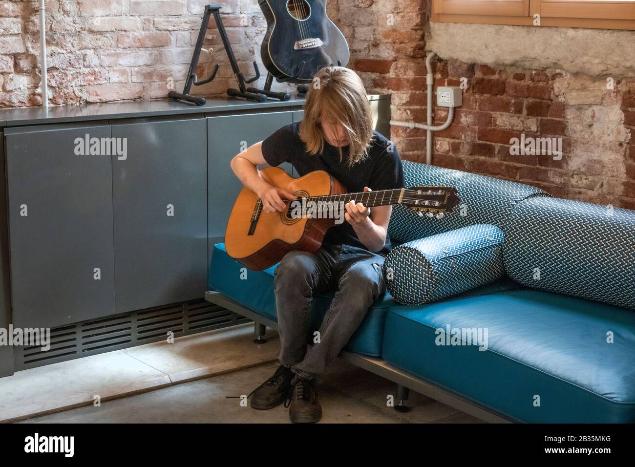 Junger Mann mit langen Haaren, der akustische Gitarre spielt. Stockfoto
