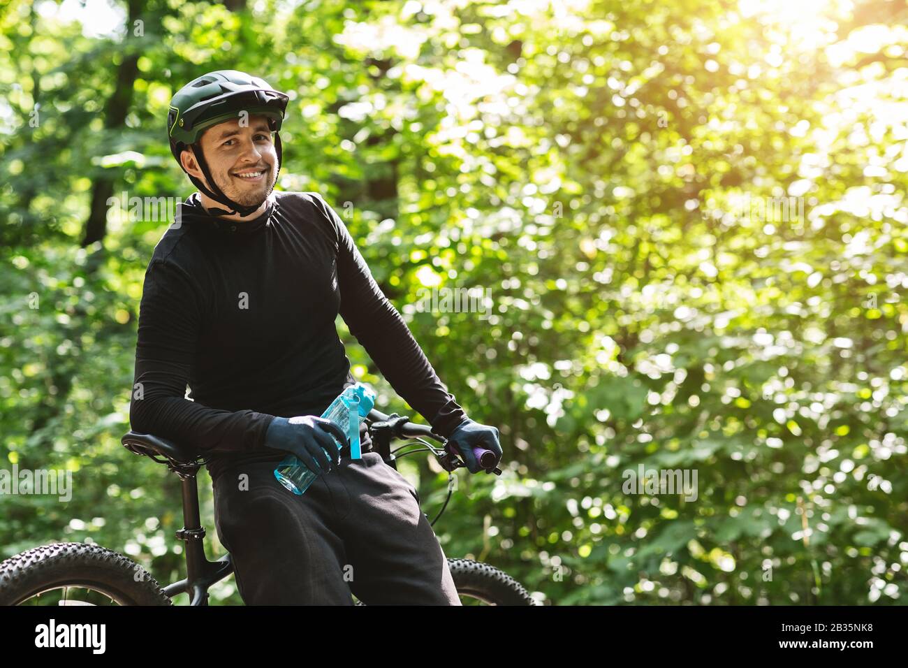 Fröhlicher Radfahrer, der eine Flasche Wasser hält und mit der Kamera lächelt Stockfoto