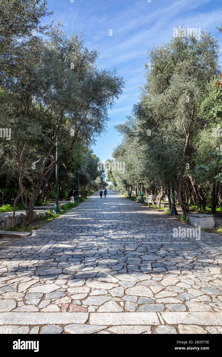 Gepflasterter Fußweg aus altem Stein am Filopappou-Hügel in Athen, Griechenland. Die Menschen gehen an einem sonnigen Tag einen Kopfsteinpflaster unter der alten Akropolis. Bäume um, ve Stockfoto