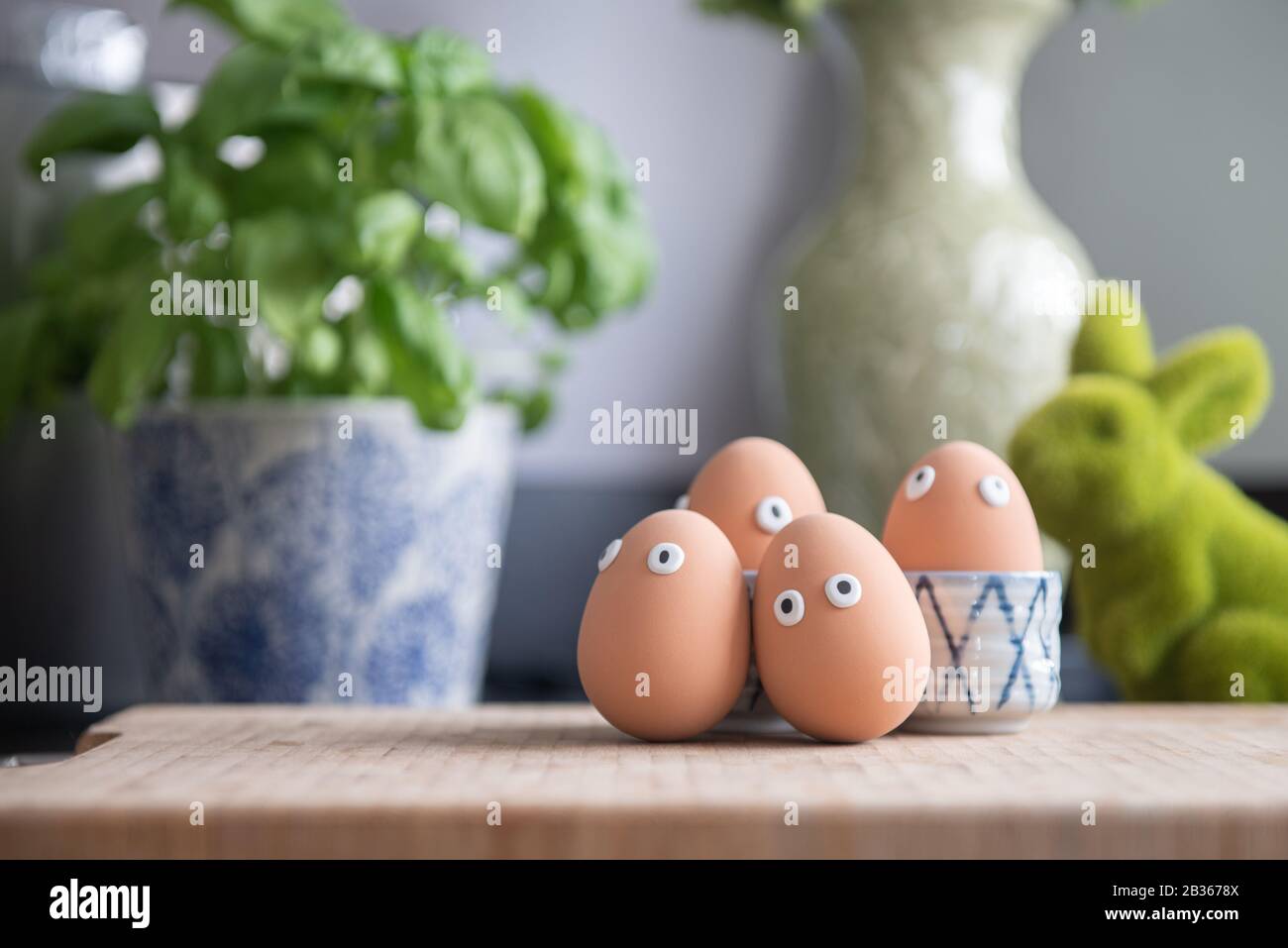 Fröhliche Ostereier in der Küche unter dem Frühlingsgras mit Blumen, Ostereierjagd, Eierfiguren mit lustigen Gesichtern, Fröhliches Osterkonzept, Küche Stockfoto