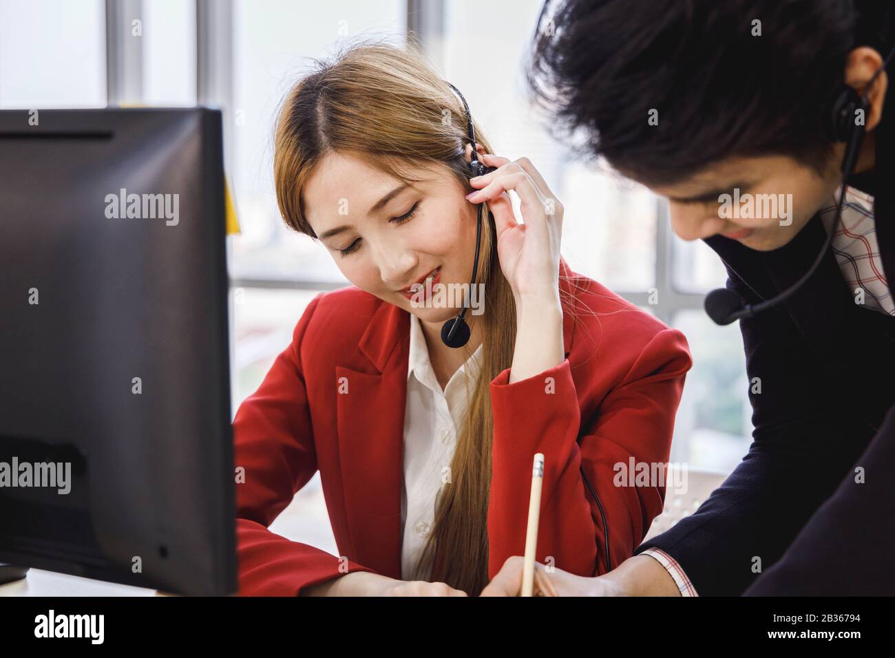 Zwei asiatische Callcenter-Agenten arbeiten zusammen und helfen sich gegenseitig. Konzept für Business, Teamarbeit, Büro-Lifestyle. Stockfoto