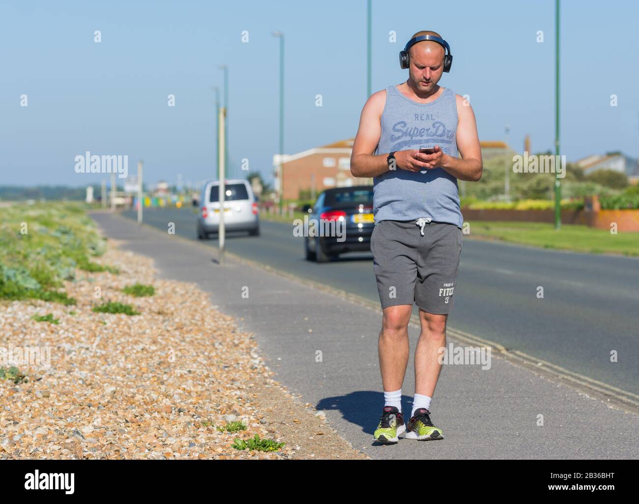 Junger Mann, der an einem warmen Frühlingstag mit Kopfhörern spazieren geht und Musik hört. Musik für unterwegs. Tragbare Musik. Stockfoto