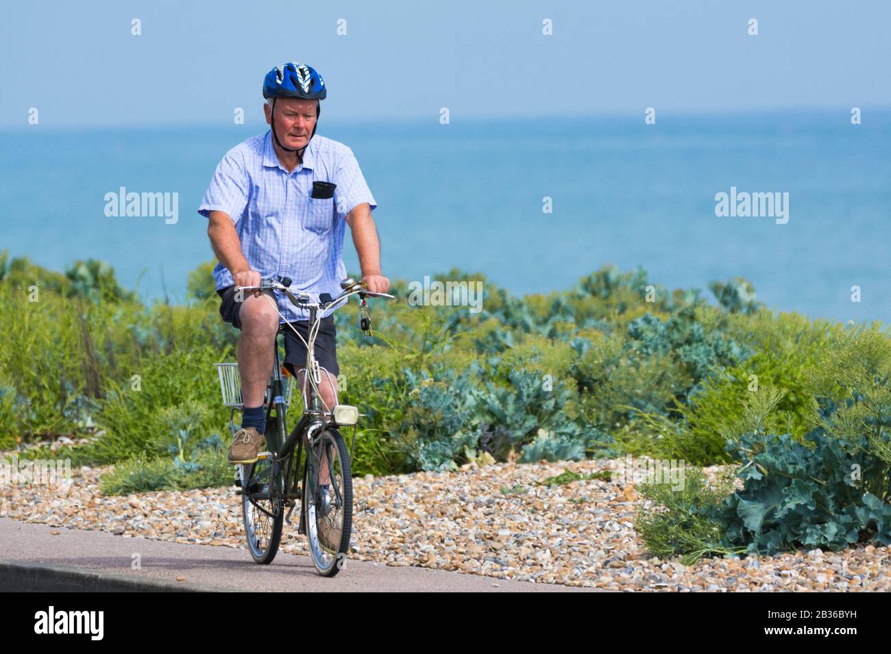 Mann mit Radhelm auf einem Gehweg am Meer mit dem Fahrrad. Radfahrer, die in Großbritannien ein Fahrrad fahren. Stockfoto