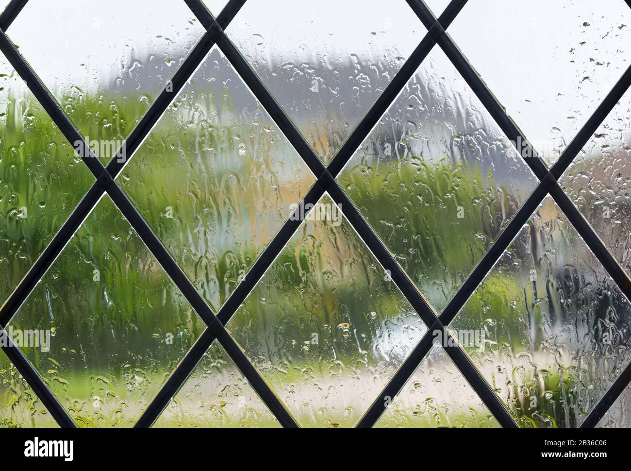Regen auf dem Fenster, wenn man draußen schaut, während er an einem nassen Tag typisch britischer Witterung regnet, um zu zeigen, wie man auf Grund von COVID19 zu Hause bleibt. Stockfoto