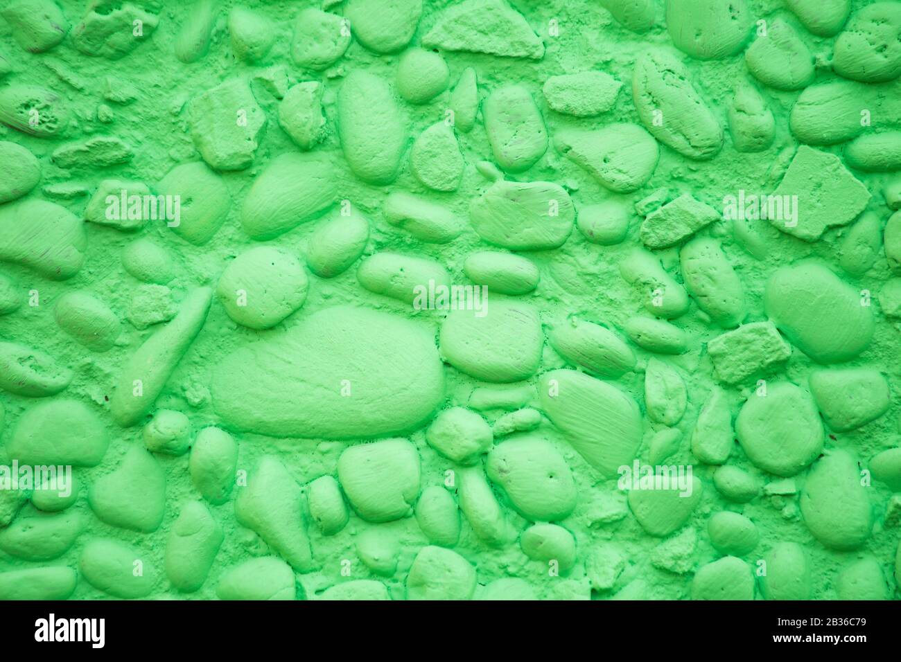 Eine Wand aus kleinen, hellgrün gestrichenen Steinen mit einer sehr markierten Textur für den Hintergrund Stockfoto