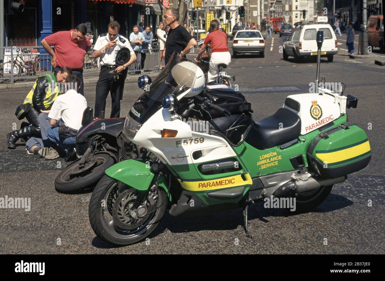 London Ambulance Service Motorrad Rettungssanitäter & Polizei unterstützen Motorradkurierfahrer, die in der Straßenlage für Verkehrsunfälle in London England UK liegen Stockfoto