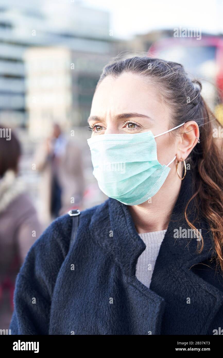 Junge Frau, die Gesichtsmaske trägt, während sie in den Straßen Londons spazieren ging Stockfoto