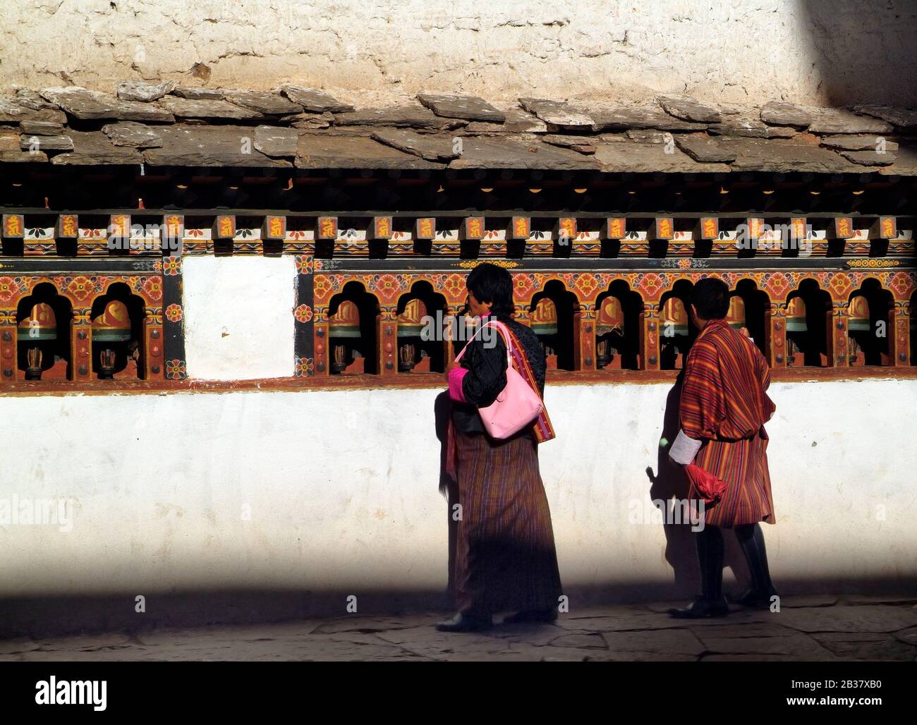 Paro, Bhutan - 18. September 2007: Bhutaner in traditioneller Kleidung an der Wand mit Gebeträdern in Paro Dzong Stockfoto