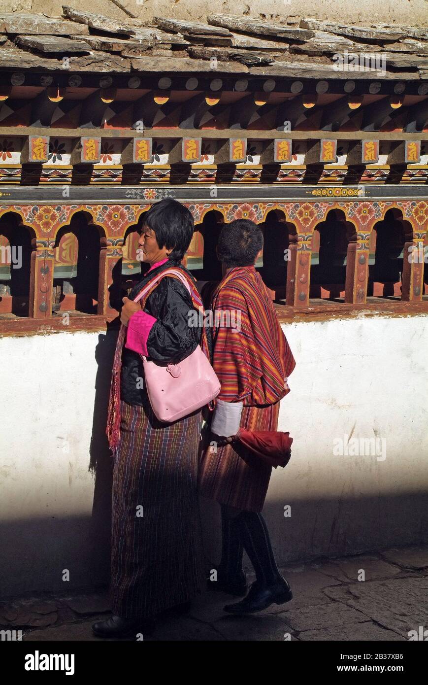 Paro, Bhutan - 18. September 2007: Bhutaner in traditioneller Kleidung an der Wand mit Gebeträdern in Paro Dzong Stockfoto