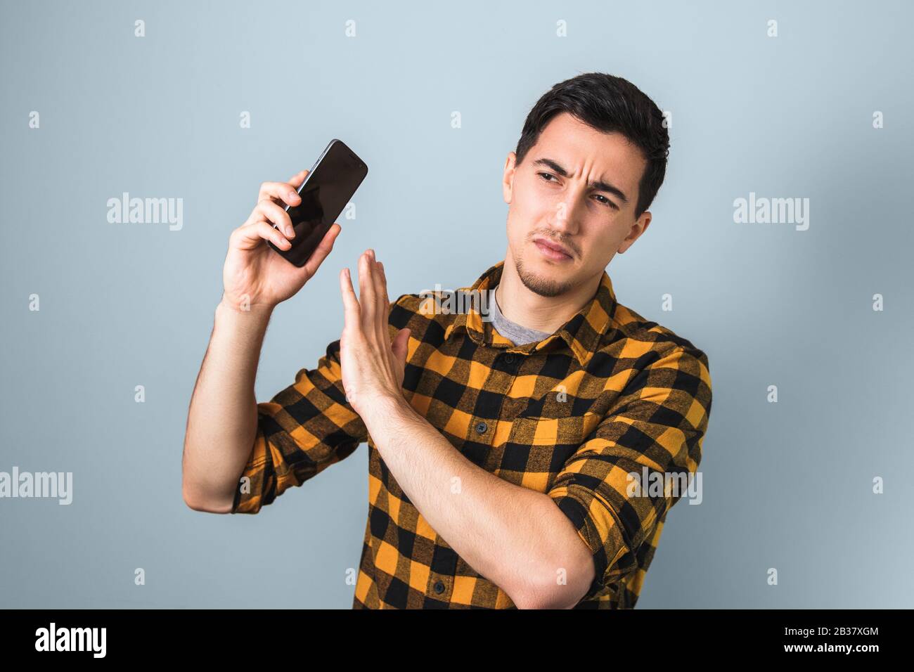 Gutaussehender Mann in gelbem Hemd ärgert sich über die Stimme eines Menschen auf dem Telefon, der mit seiner Hand gestikuliert wurde, die nicht mehr sagt Stockfoto