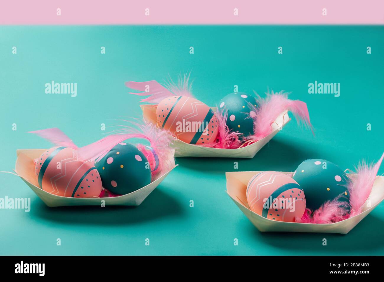 Farbige verzierte Eier mit Feder in Bambusgerichten sehen aus wie Boote auf neominzfarbenem und rosafarbenem Hintergrund. Konzept von Ostern, Null Abfall, Ökologie Stockfoto
