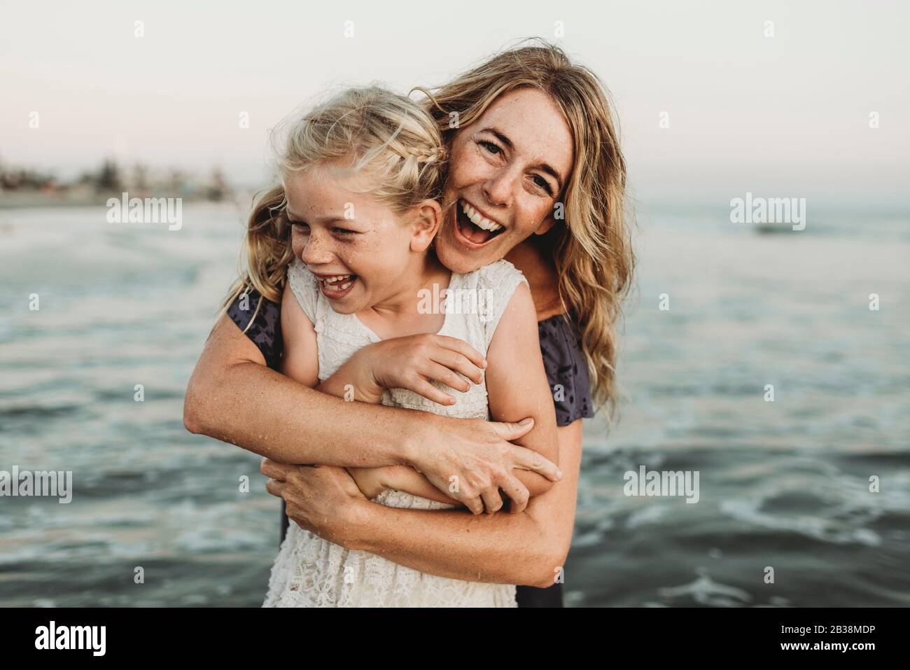 Mutter umarmt junge Mädchen mit Sommersprossen im Ozean lachen Stockfoto