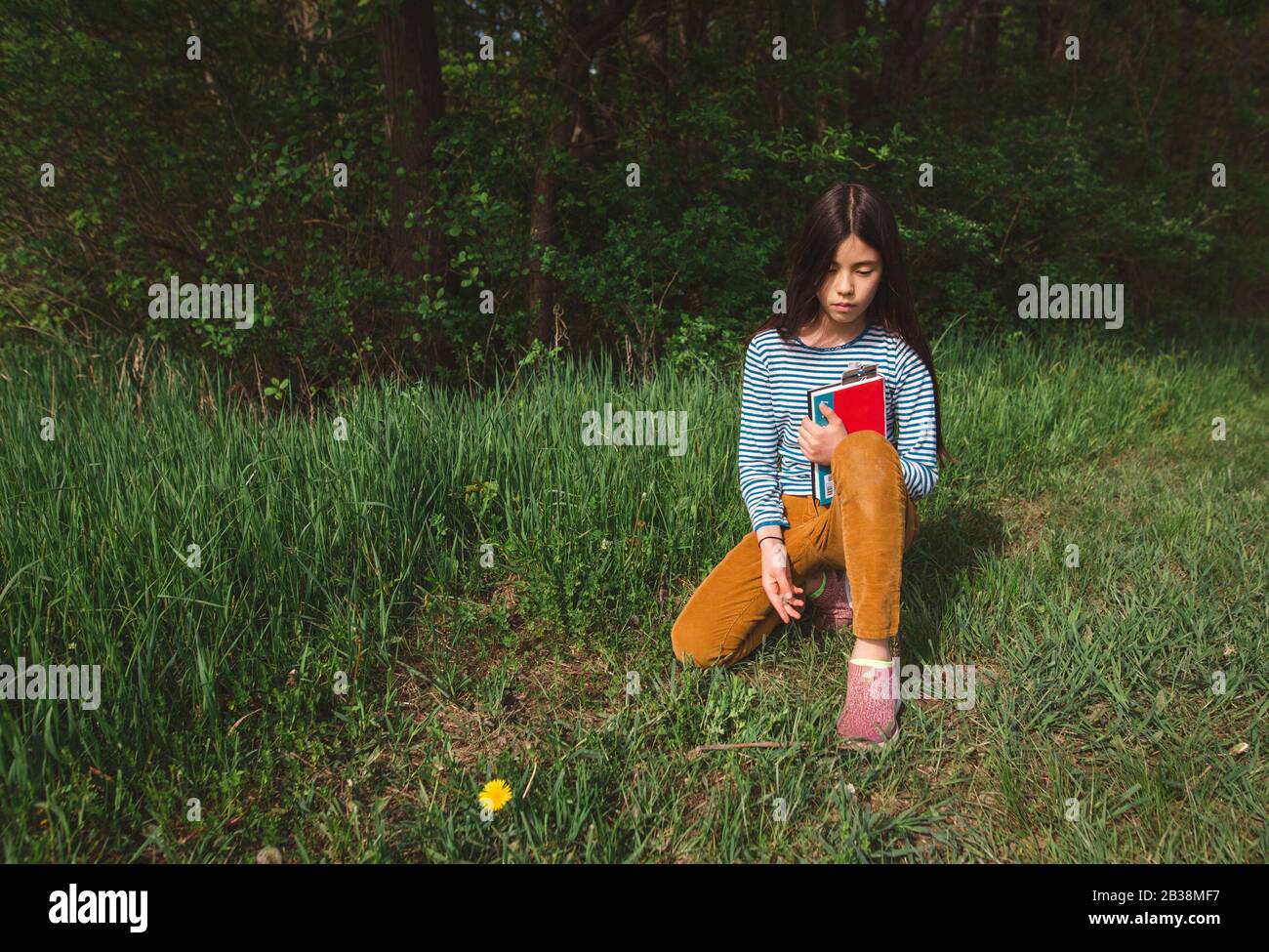 Ein nachdenkliches Mädchen sitzt ruhig mit einem Buch in hohem Gras im Frühling Stockfoto
