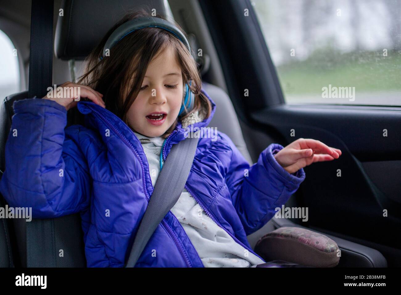 Ein kleines Mädchen hört auf einer Autofahrt Musik über Kopfhörer Stockfoto
