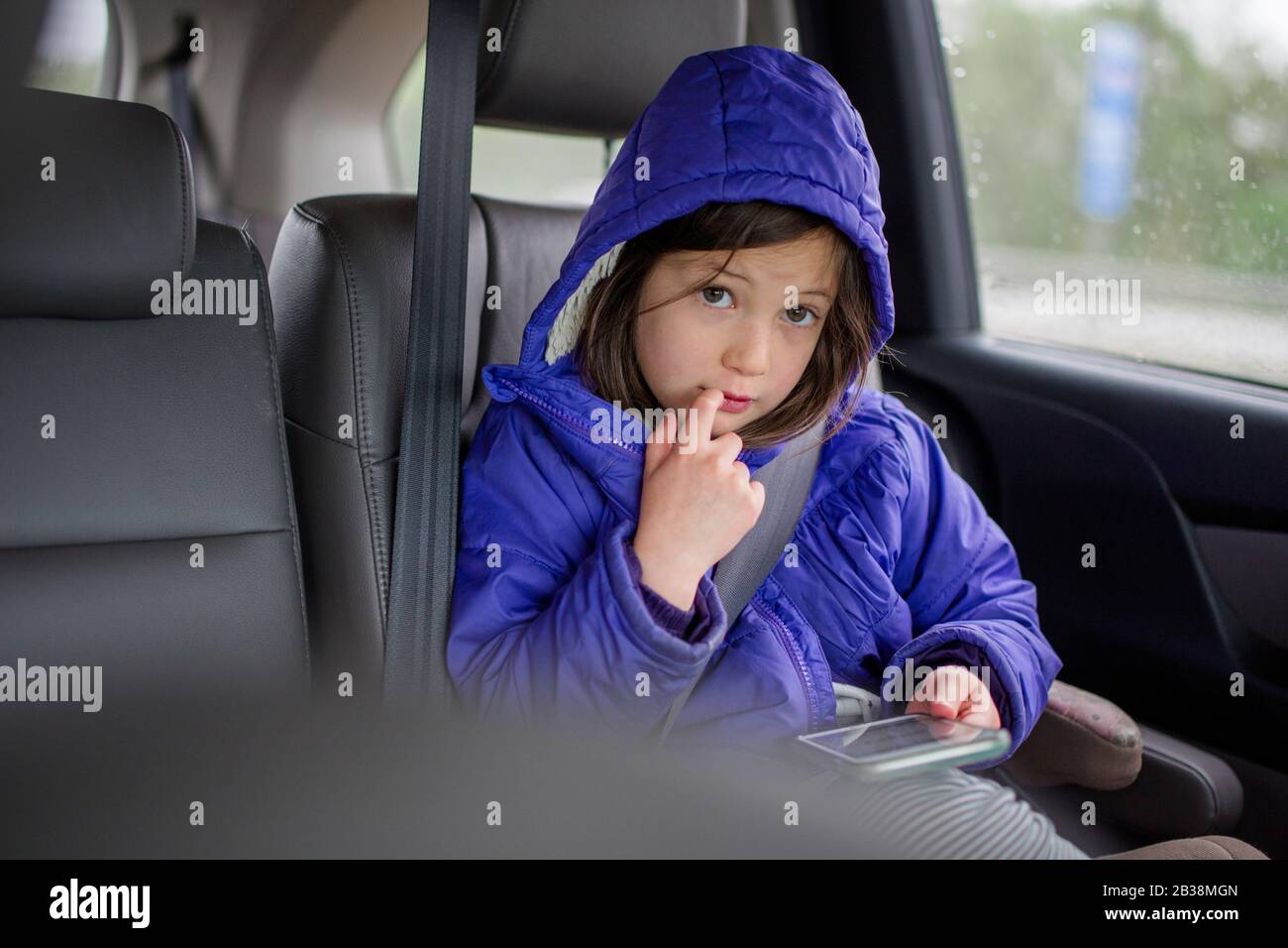 Ein kleines Mädchen auf dem Rücksitz eines Autos blickt von einem Telefon auf Stockfoto