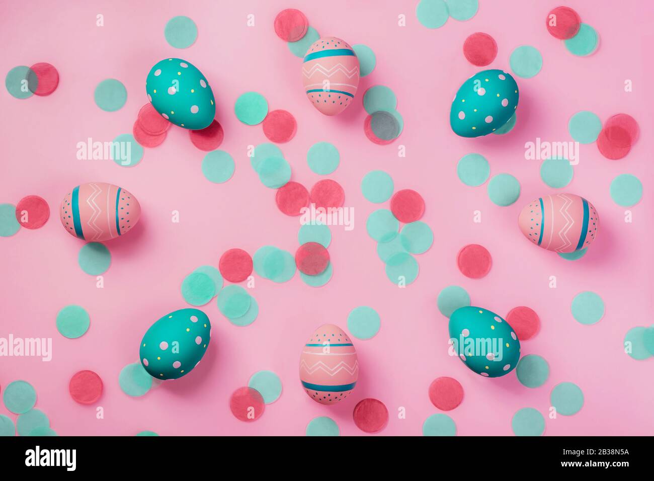 Pinkfarbene und minzfarbene verzierte Eier auf pinkfarbenem Hintergrund mit Konfetti. Osterkonzept, Naturrahmen mit Kopierraum Stockfoto