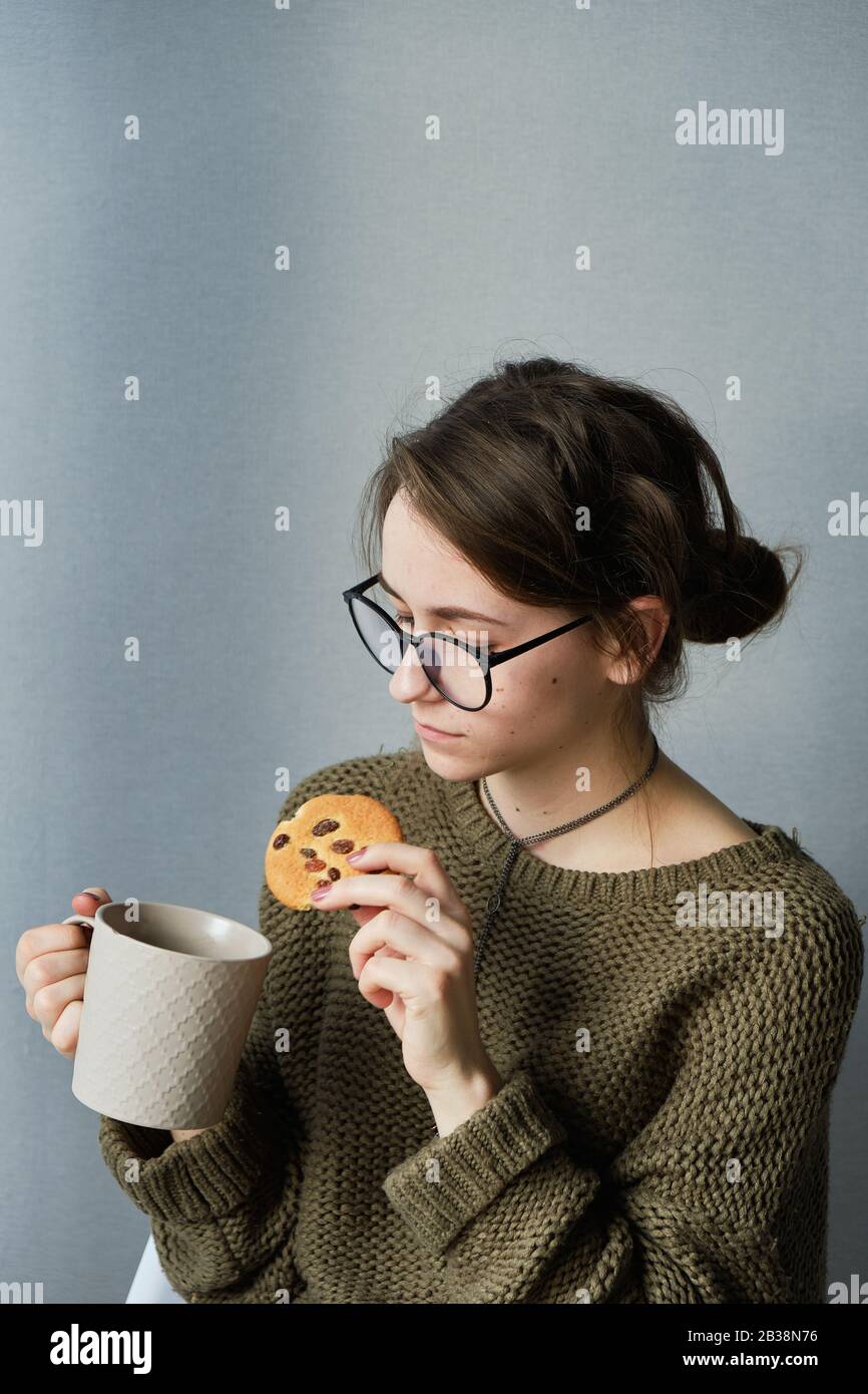 Tausendjährige braunhaarige Mädchen in Gläsern trinken Tee mit Kuchen allein Stockfoto