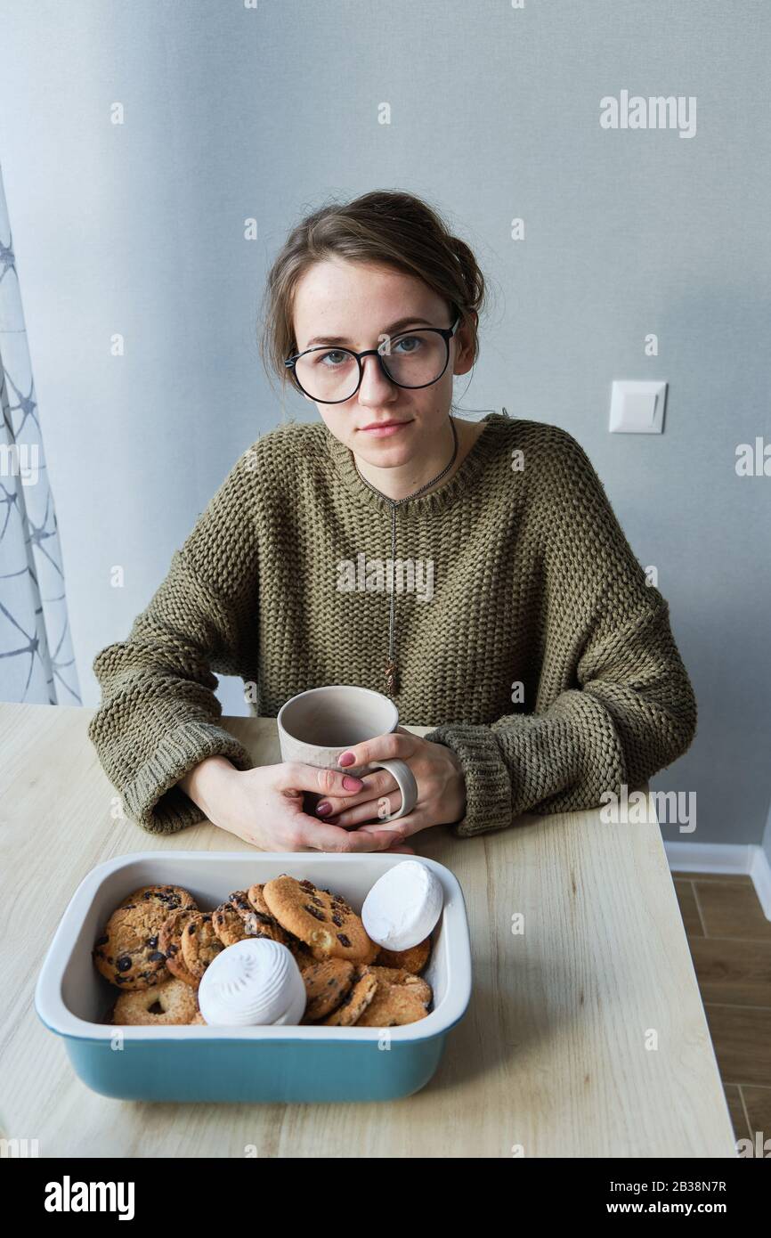 Tausendjährige braunhaarige Mädchen trinkt Tee mit Kuchen allein Stockfoto