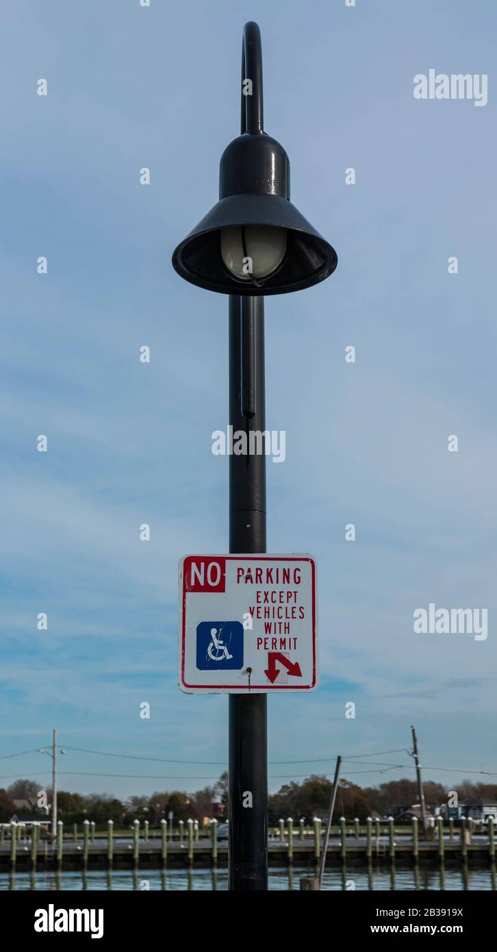 Eine Lampenpost an einem örtlichen Yachthafen hat ein Schild mit der Aufschrift "No Parking except vehicles with permit, for behind boaters to Park." Stockfoto