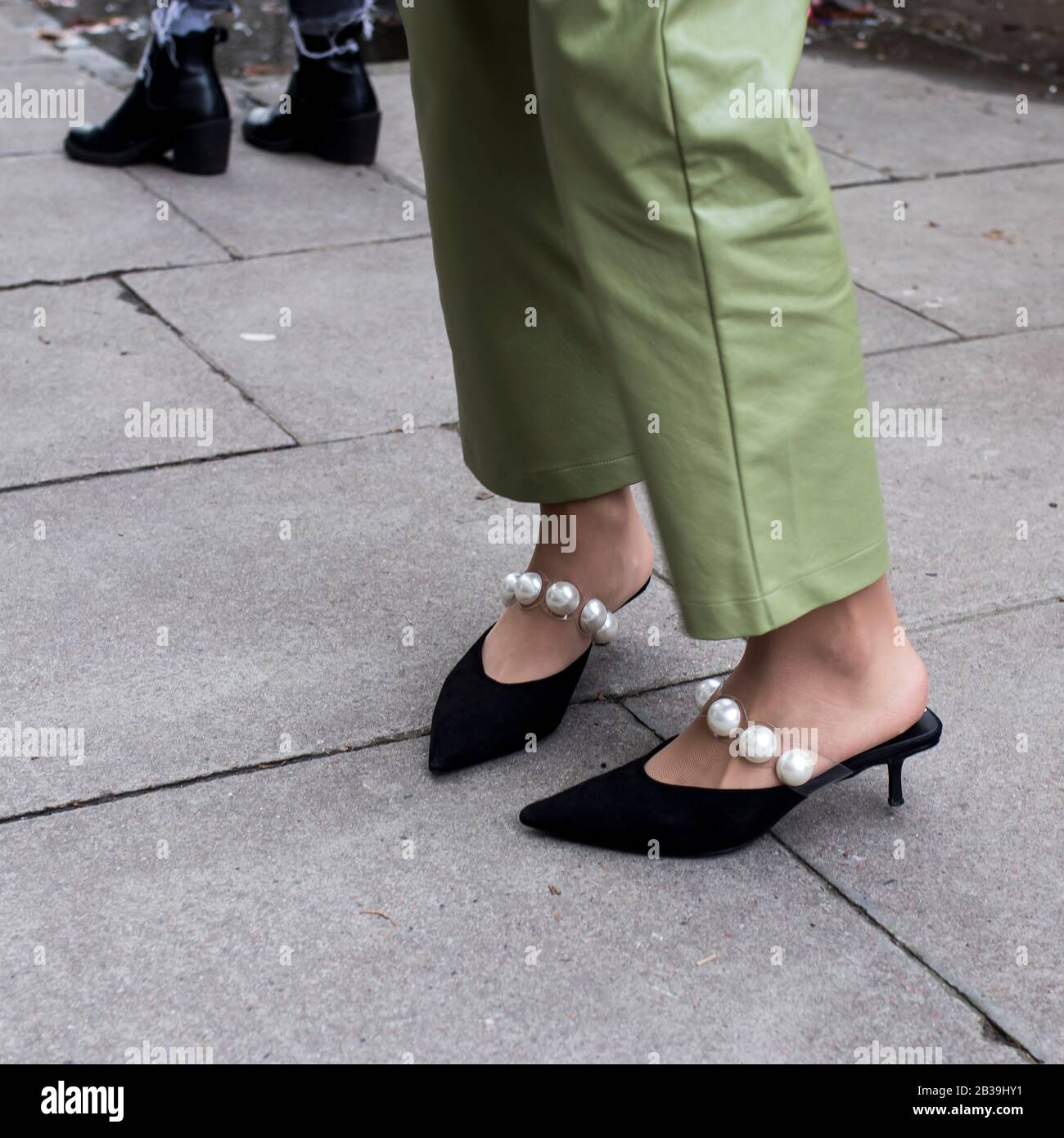 Ein Mädchen in hellgrünem Hosenanzug in transparenten Strumpfhosen mit großen Perlen und spitzen schwarzen Stilettos. Stockfoto